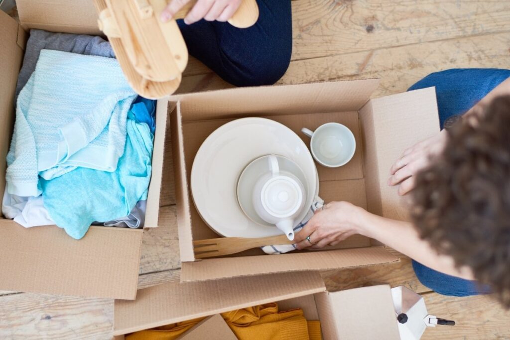Packing dishes and kitchen items with towels inside a moving box.